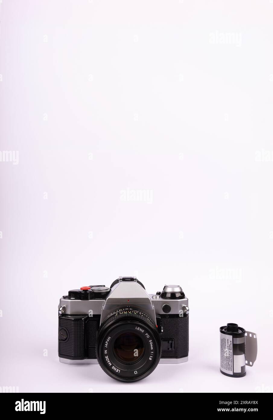 Una fotocamera tradizionale e rotoli di pellicola da 35 mm posizionati centralmente su uno sfondo bianco in un layout verticale. Enfatizza le attrezzature fotografiche retrò. Foto Stock