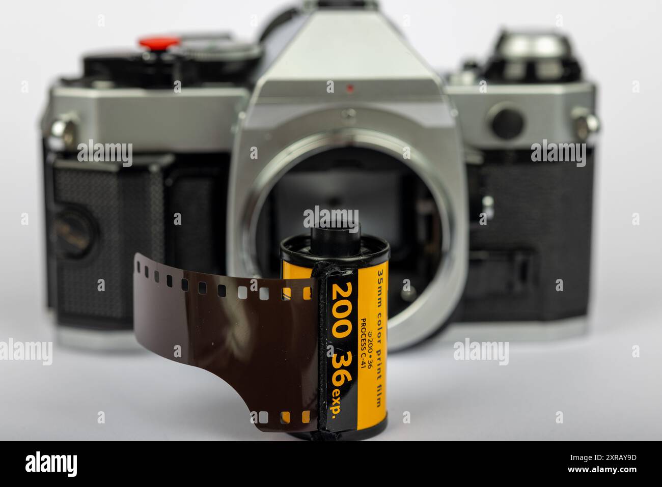 Vista dettagliata di un rotolo di pellicola da 35 mm a fuoco, con una vecchia fotocamera senza lente sfocata sullo sfondo. Lo sfondo bianco accentua l'aspetto classico. Foto Stock