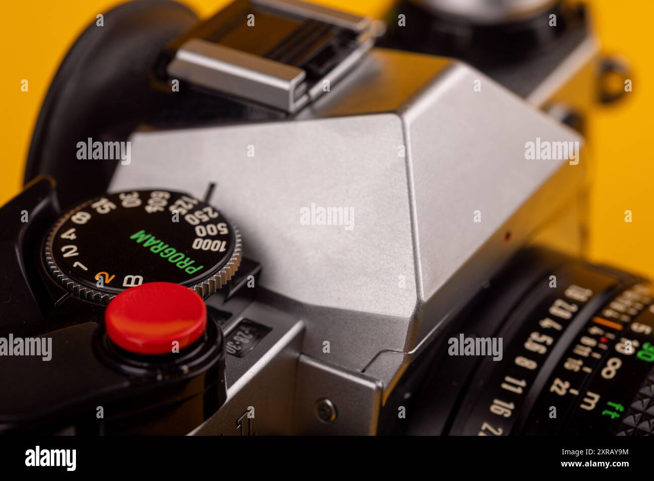 Primo piano di una fotocamera vintage con pulsante dell'otturatore rosso, evidenziato su uno sfondo giallo brillante. Concentrati sul design classico. Foto Stock