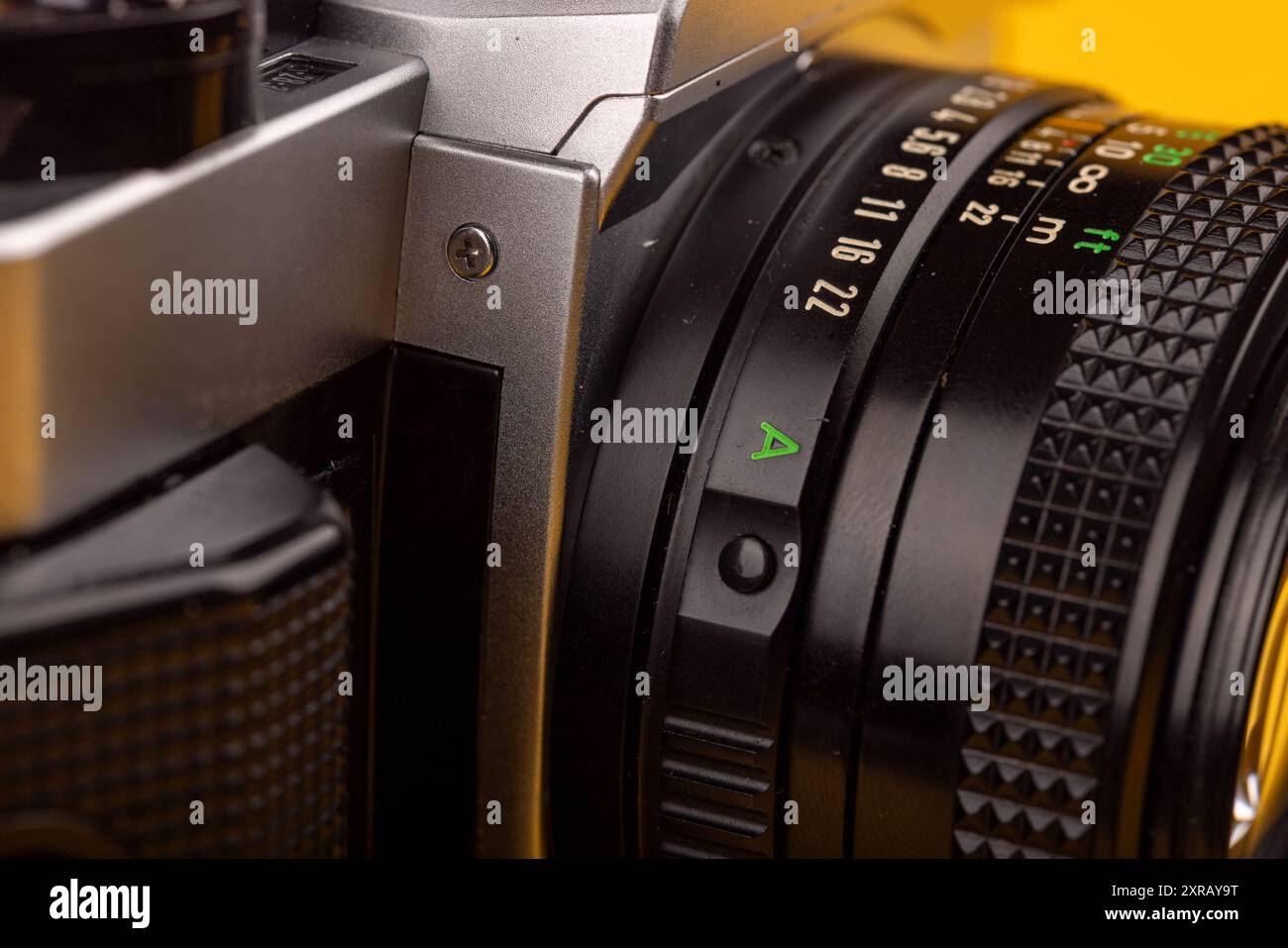 Vista dettagliata dell'obiettivo di una vecchia fotocamera, evidenziandone il design intricato e la maestria artigianale. Si trova su uno sfondo giallo brillante. Foto Stock