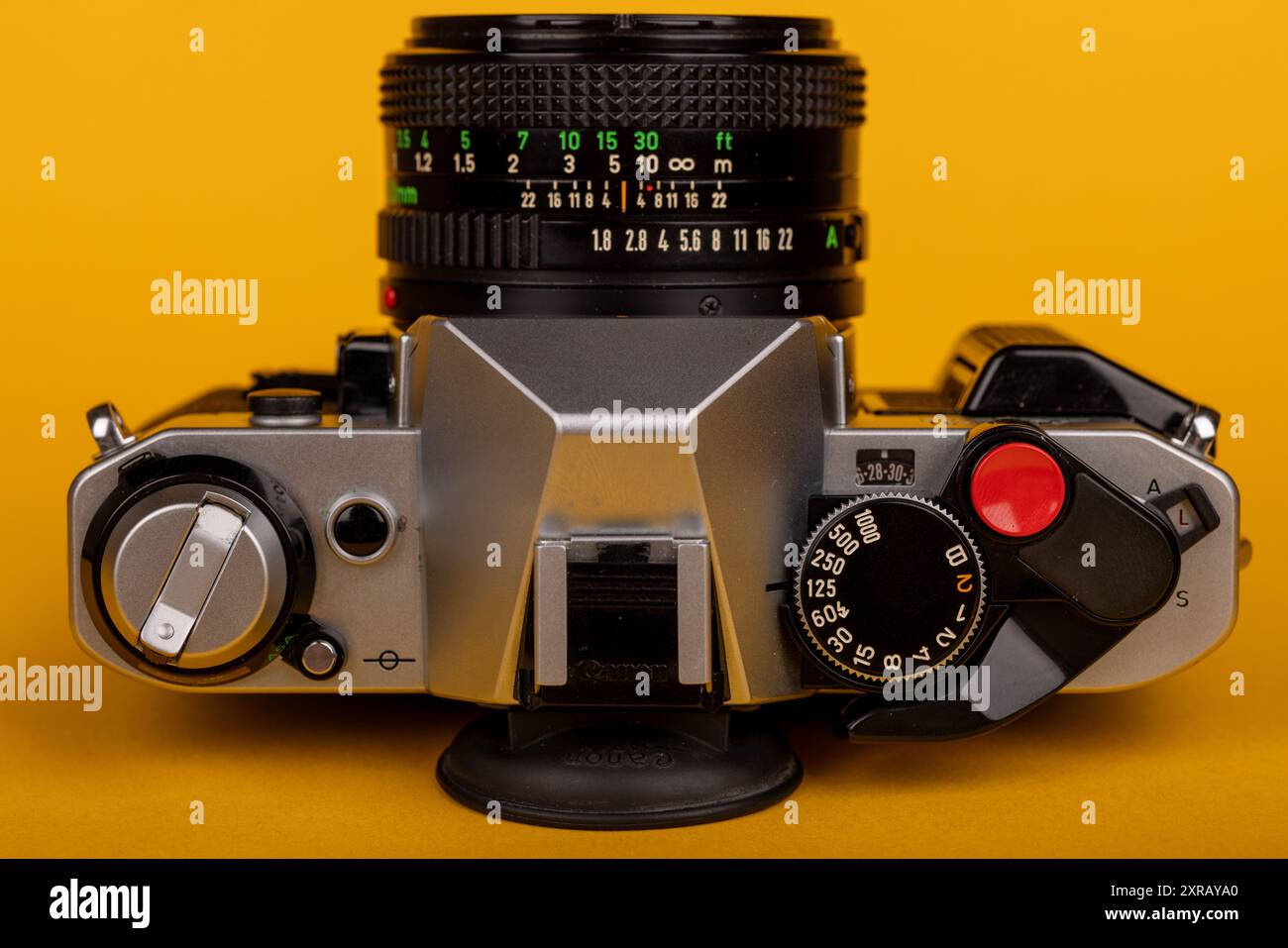 Primo piano di una fotocamera antica distesa sul retro con l'obiettivo rivolto verso l'alto, concentrandosi sui comandi su uno sfondo giallo. Classico e dettagliato Foto Stock