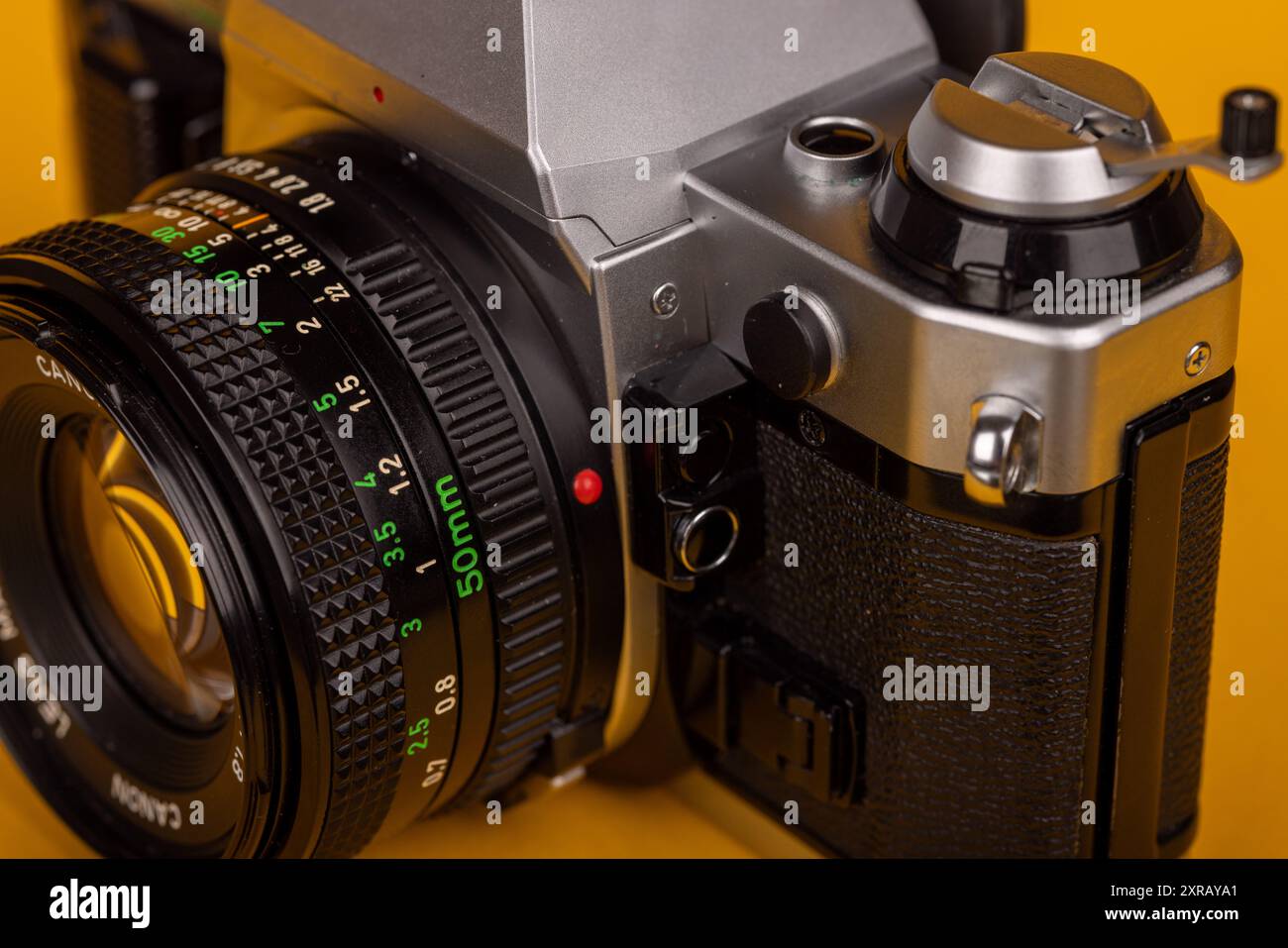 Vista dettagliata dell'obiettivo di una fotocamera vintage, in contrasto con lo sfondo giallo. Enfatizza il design intricato e la nostalgia. Foto Stock