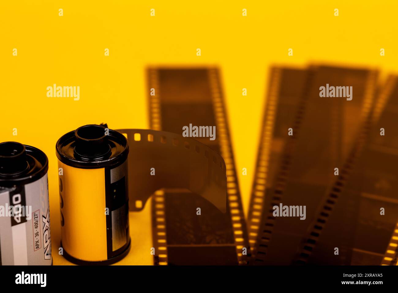 Primo piano di rotoli di pellicola analogica con pellicola sviluppata disposta su una superficie gialla brillante. Un omaggio alla fotografia d'epoca Foto Stock