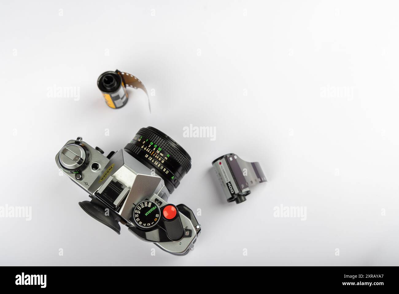 Vista dall'alto di una fotocamera antica e rotoli di pellicola da 35 mm su una superficie bianca. La fotocamera vintage è allineata a sinistra e presenta un design senza tempo. Foto Stock