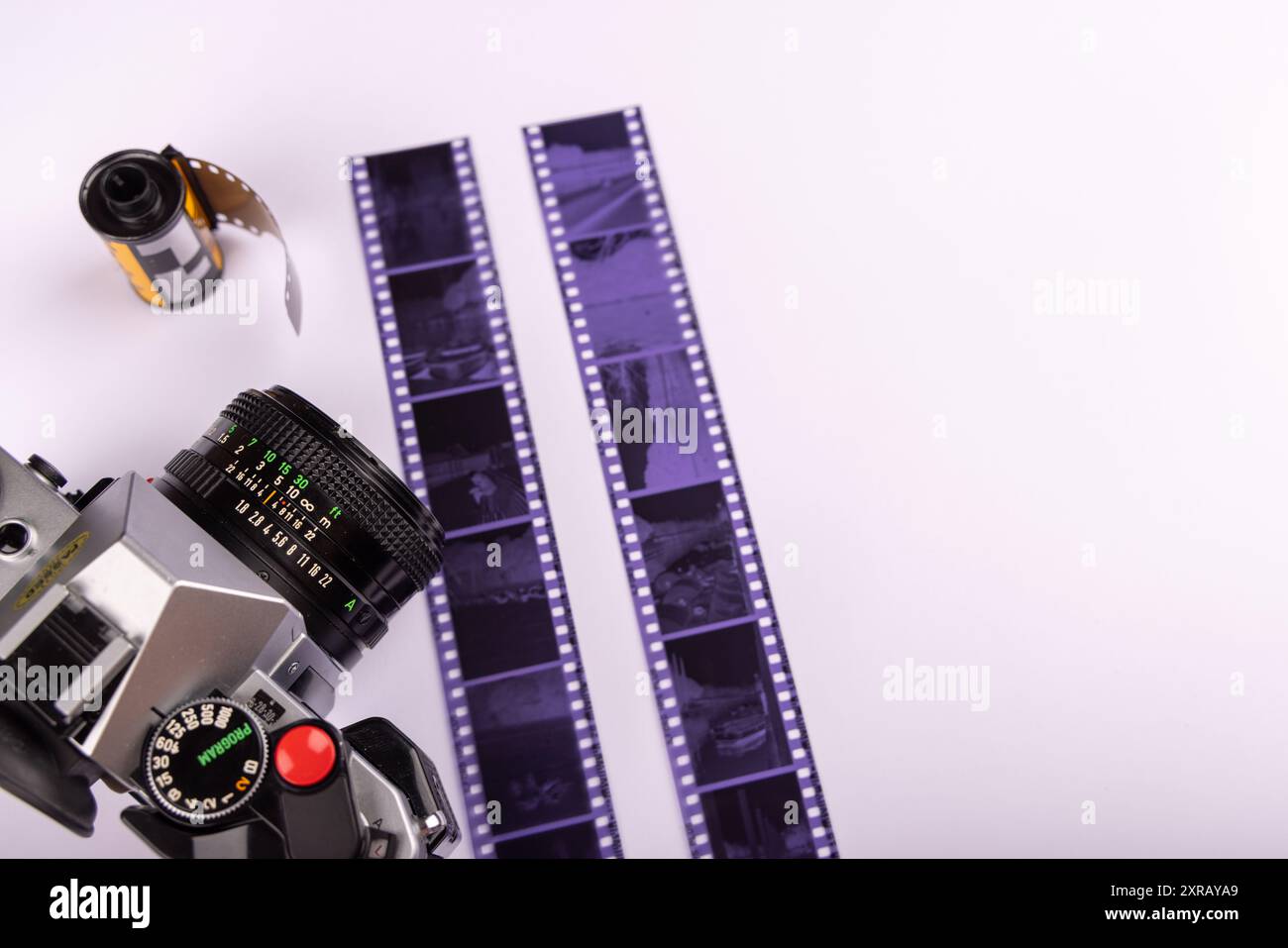 Fotocamera antica e rotoli di pellicola da 35 mm, con pellicola sviluppata, disposti su uno sfondo bianco. La telecamera è posizionata a sinistra, vista dall'alto. Foto Stock