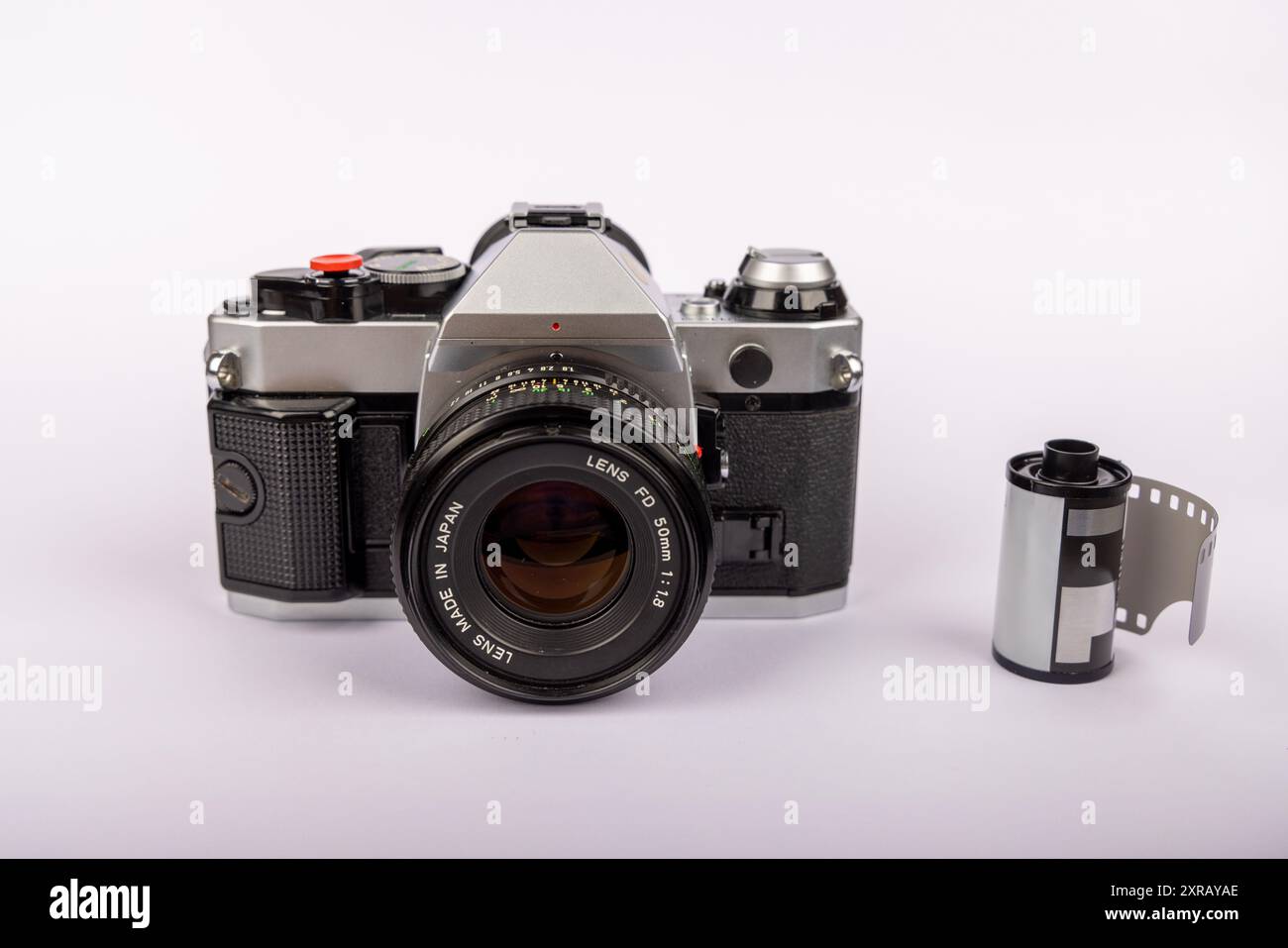 Fotocamera antica posizionata al centro di uno sfondo bianco, con diversi rotoli di pellicola da 35 mm disposti intorno ad esso. Evoca un'era fotografica classica. Foto Stock