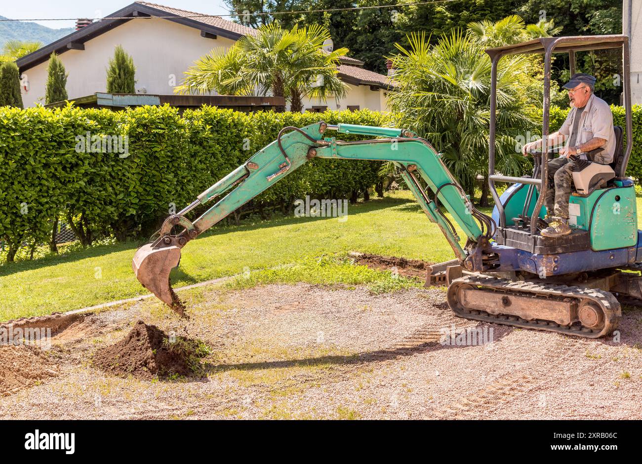 Un lavoratore su un mini escavatore sta scavando il terreno davanti alla casa. Lavori di pavimentazione e pavimentazione esterna. Foto Stock