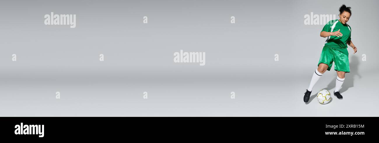 Una donna atletica con una divisa da calcio verde manovra sapientemente la palla in un ambiente da studio. Foto Stock