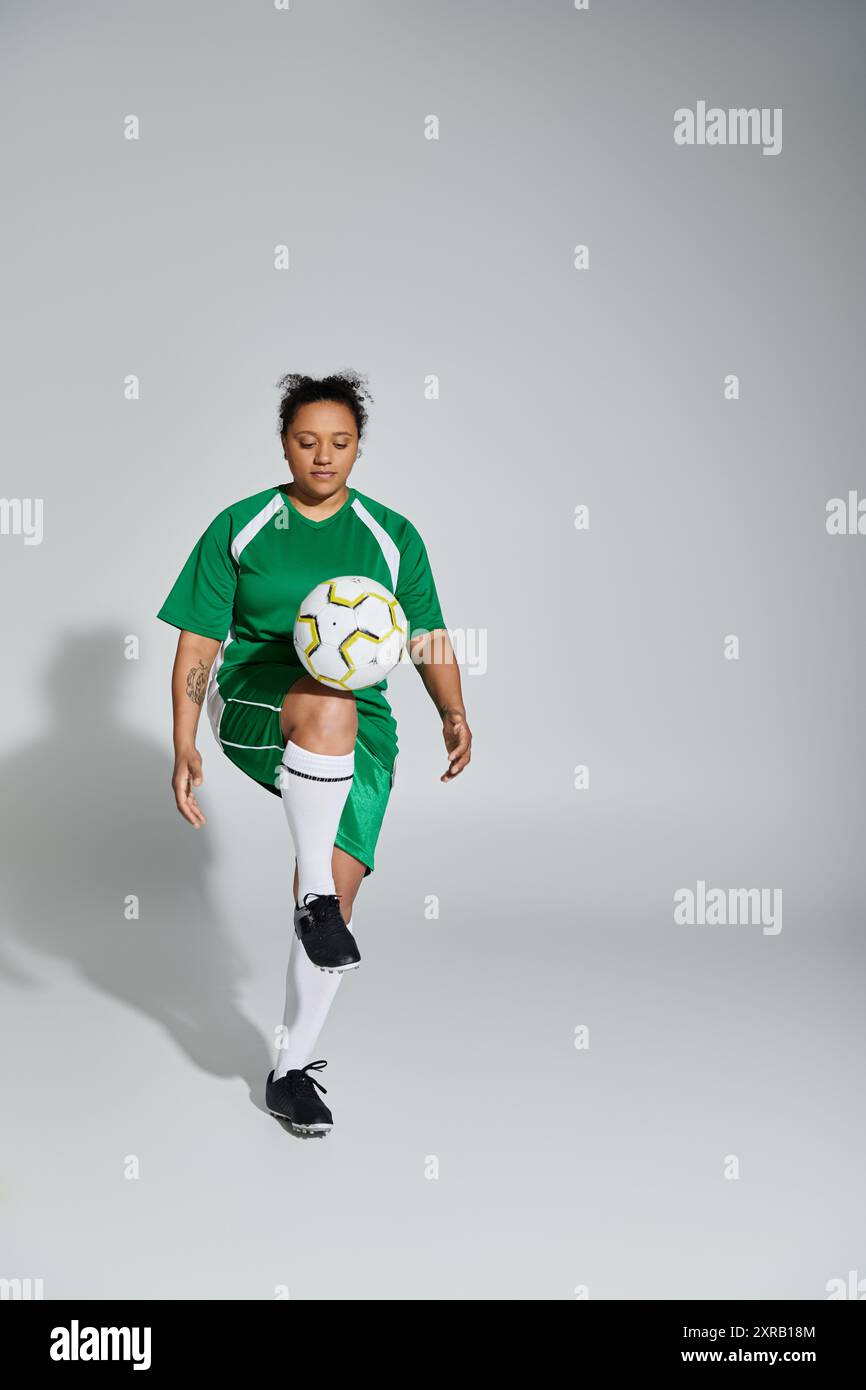 Una donna con una maglia verde giocherà abilmente con un pallone da calcio in un ambiente da studio. Foto Stock