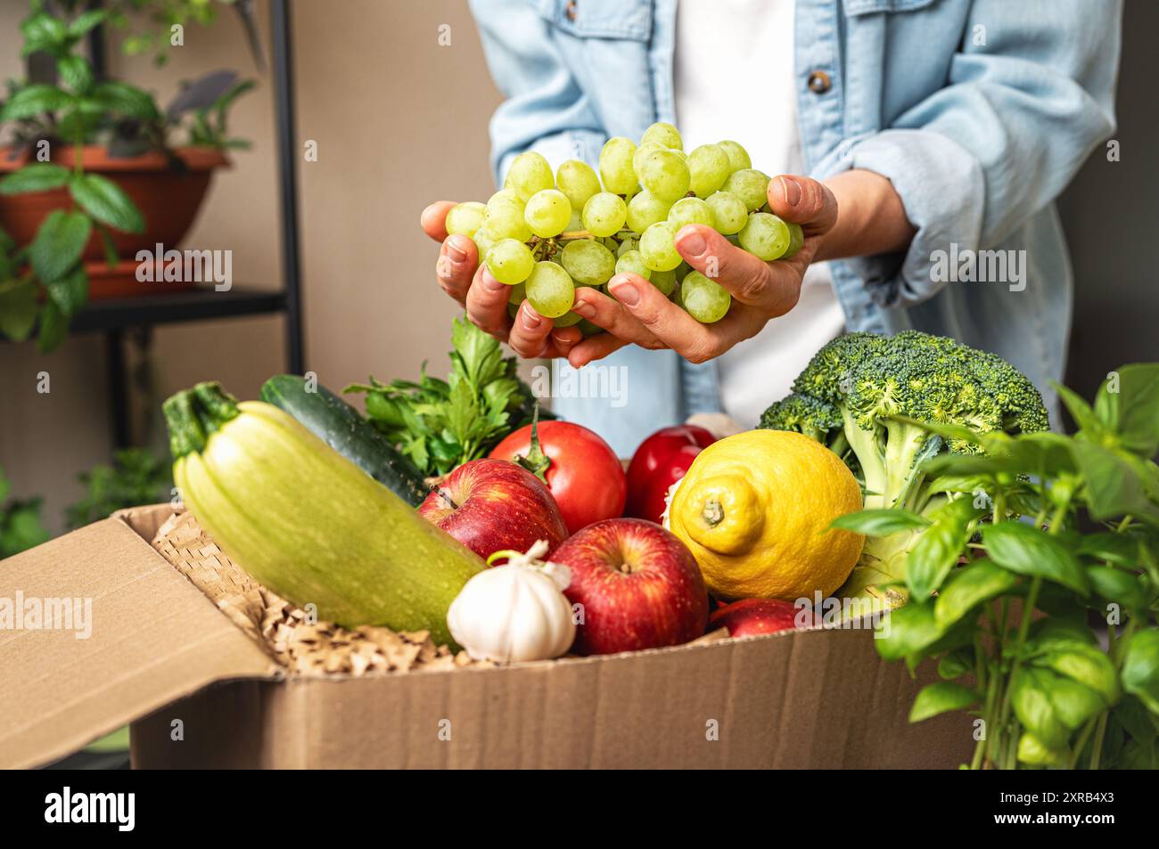 Persona che disimballa online ordinando frutta e verdura coltivate in azienda, tenendo in mano uva bianca. Foto Stock