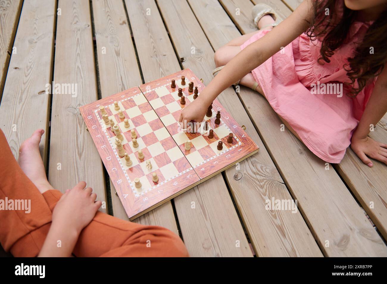 Vista dall'alto dei bambini che giocano a scacchi insieme su un ponte di legno. Un bambino sta facendo una mossa, mentre un altro osserva il gioco con attenzione. Foto Stock