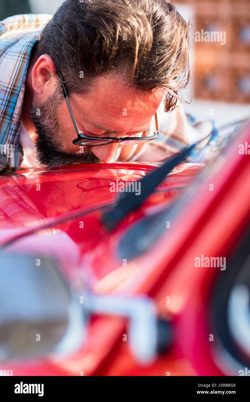 L'uomo bacia la sua nuova auto. Amanti dell'automobile e proprietario che abbraccia il suo veicolo. Concetto di sogni e acquisto. Ragazzo soddisfatto con gli occhi chiusi che abbraccia l'auto Foto Stock