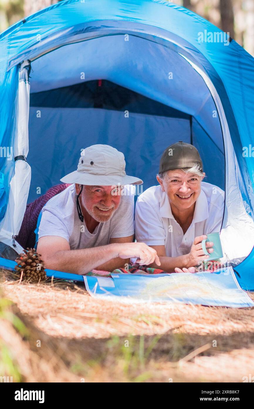 Una coppia di anziani viaggiatori attivi si diverte insieme all'interno di una tenda in campeggio gratuito nella foresta - giovani pensionati e un concetto di stile di vita alternativo gratuito con amore per la natura - viaggeranno la vita a ogni età Foto Stock