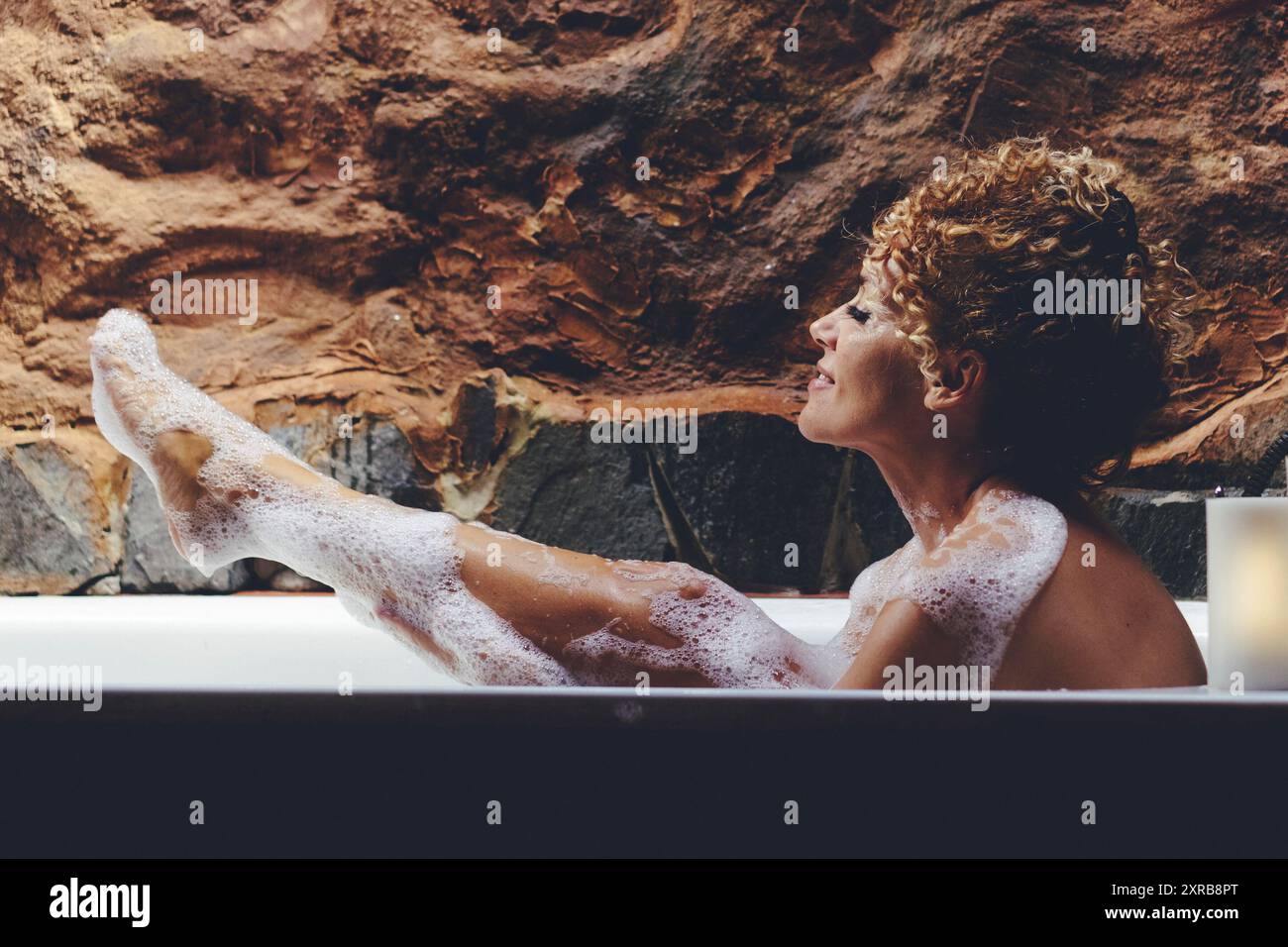 Una donna che si diverti a fare il bagno di sopa a bolle nel bagno di casa. Concetto di cura del corpo e trattamento della pelle. Sorridere e divertirsi lavando nel tubo. Concetto di depilazione delle gambe Foto Stock