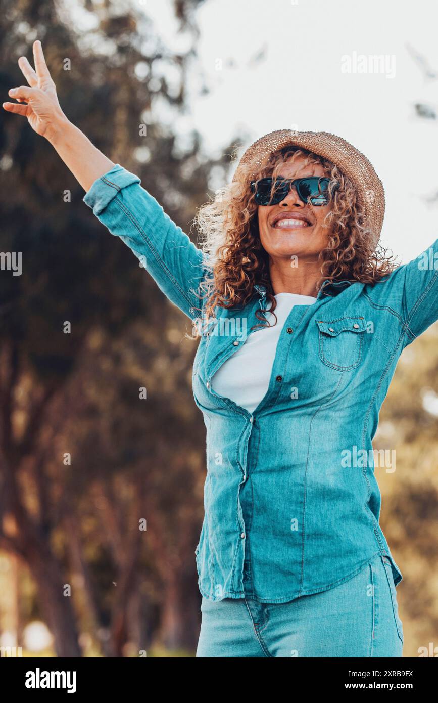 Gente overjoyed donna felice alzando le braccia con il gesto di vittoria e sorridendo con gli alberi verdi natura all'aperto sfondo. Allegre donne in attività turistiche fuori. Signora che si diverte Foto Stock