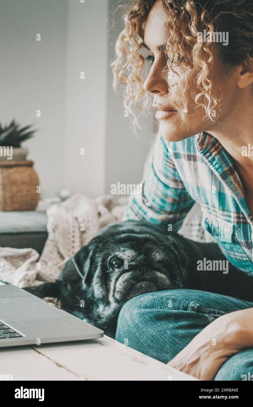 Donna che lavora su un notebook si è concentrata a guardare lo schermo. Bel cane che si rilassa. Concetto di persone moderne e migliore amico animale. Le donne possono divertirsi online utilizzando il computer. Persone e cani Foto Stock
