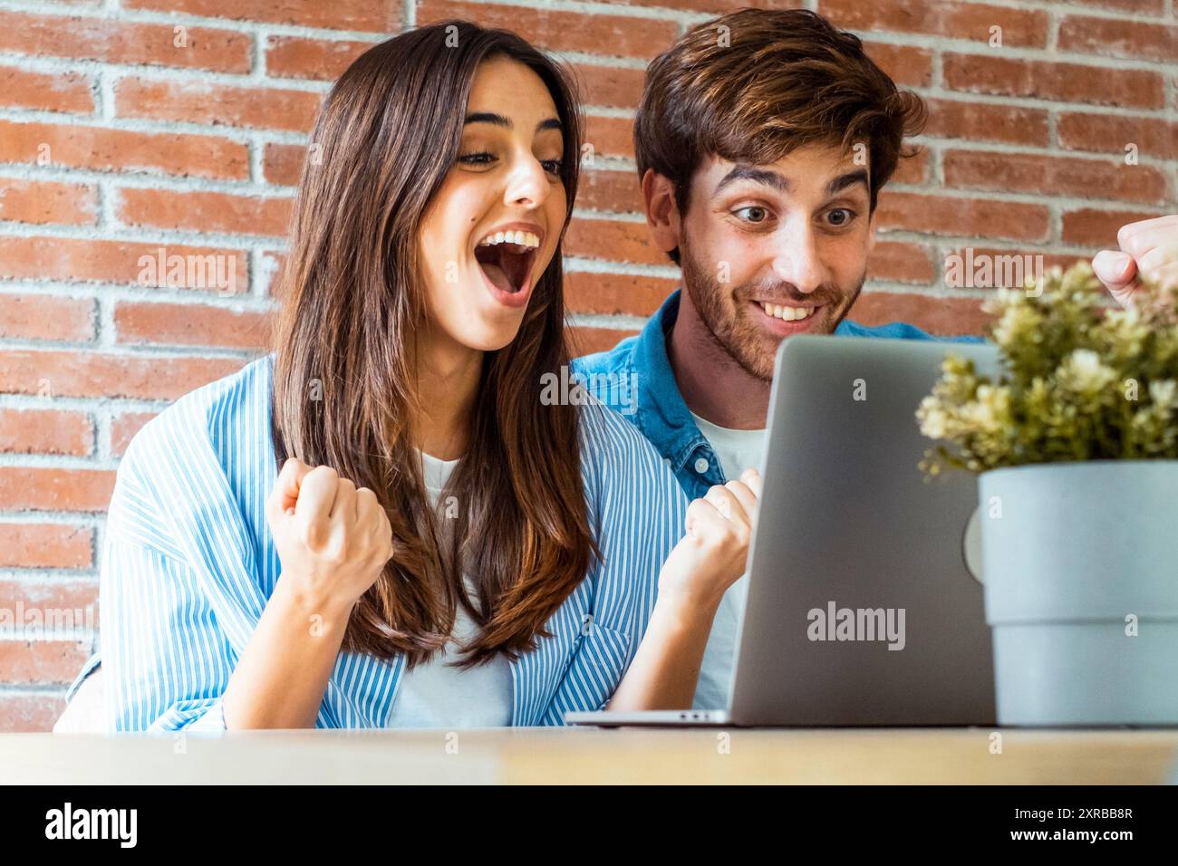 Una giovane coppia di adulti davanti a un notebook con un gesto e un'espressione gioiosa e felice. Concetto di successo professionale per uomini e donne e aziende online stile di vita per piccole imprese a casa Foto Stock
