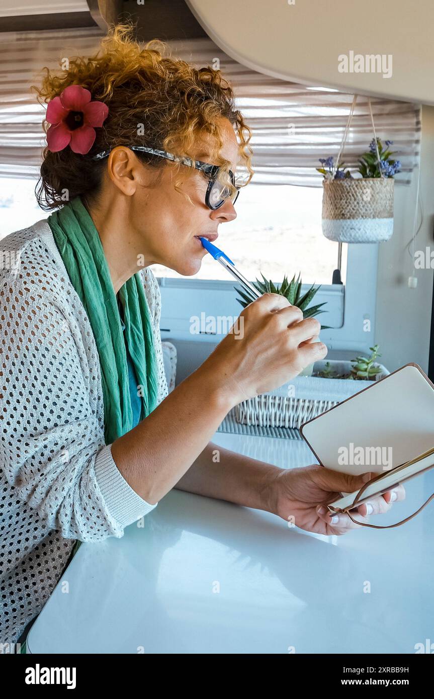 Una donna adulta che legge e scrive appunti all'interno di un camper. Persone moderne viaggiatore di stile di vita e concetto di lavoro a distanza. Bella signora matura che si diverte a noleggiare un camper da sola per le vacanze Foto Stock