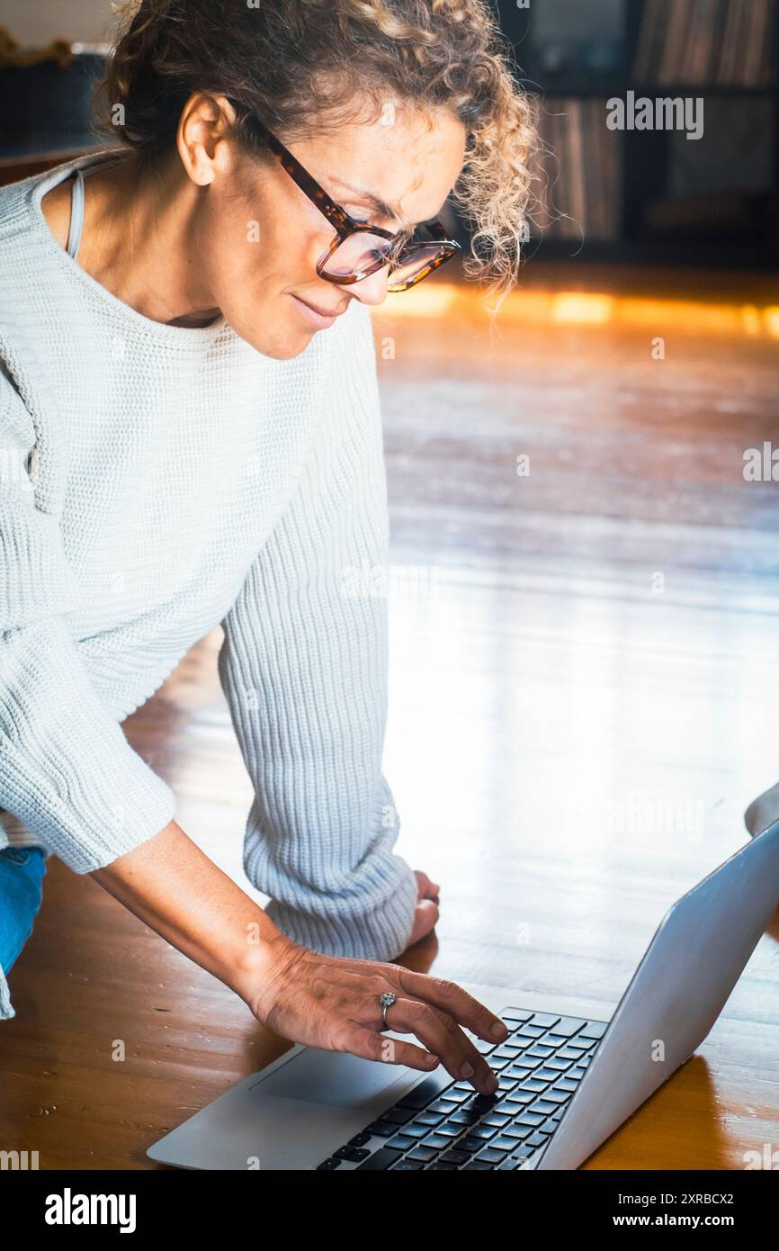 Donna concentrata che usa il notebook a casa mentre siede a terra, donna adulta che lavora al computer online, scrive e-mail, lavora come freelance, mockup. Una donna che utilizza il computer per attività ricreative al chiuso Foto Stock