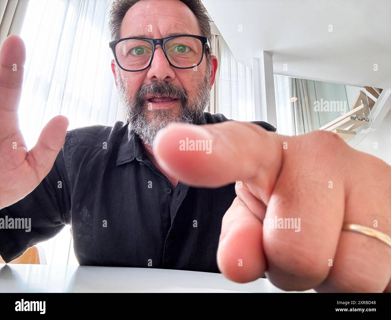 Un uomo adulto impegnato in una videoconferenza puntando il dito sullo schermo nella vista della telecamera. Persone e comunicazioni online con webcam su laptop o dispositivo telefonico. Un moderno uomo d'affari che viaggia da remoto Foto Stock