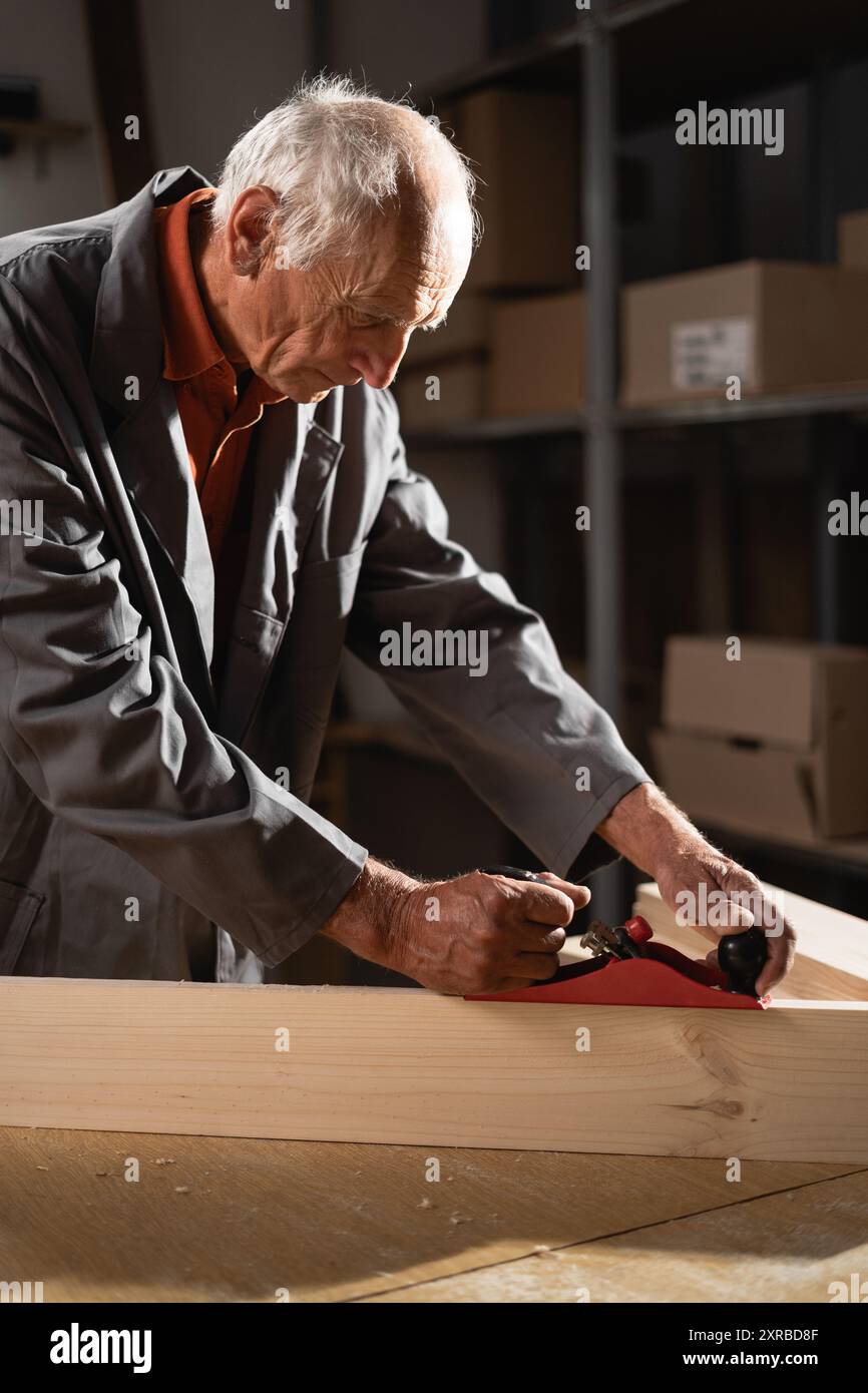 Falegname che utilizza una pialla manuale per la lavorazione del legno nella sua officina. Abile artigiano che lavora con il legno per creare precisi oggetti in legno, dimostrando Foto Stock