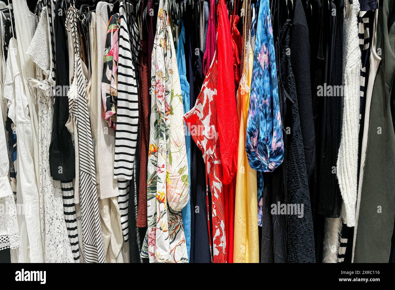 Un assortimento colorato di vari capi di abbigliamento appesi su un rack in un negozio Foto Stock