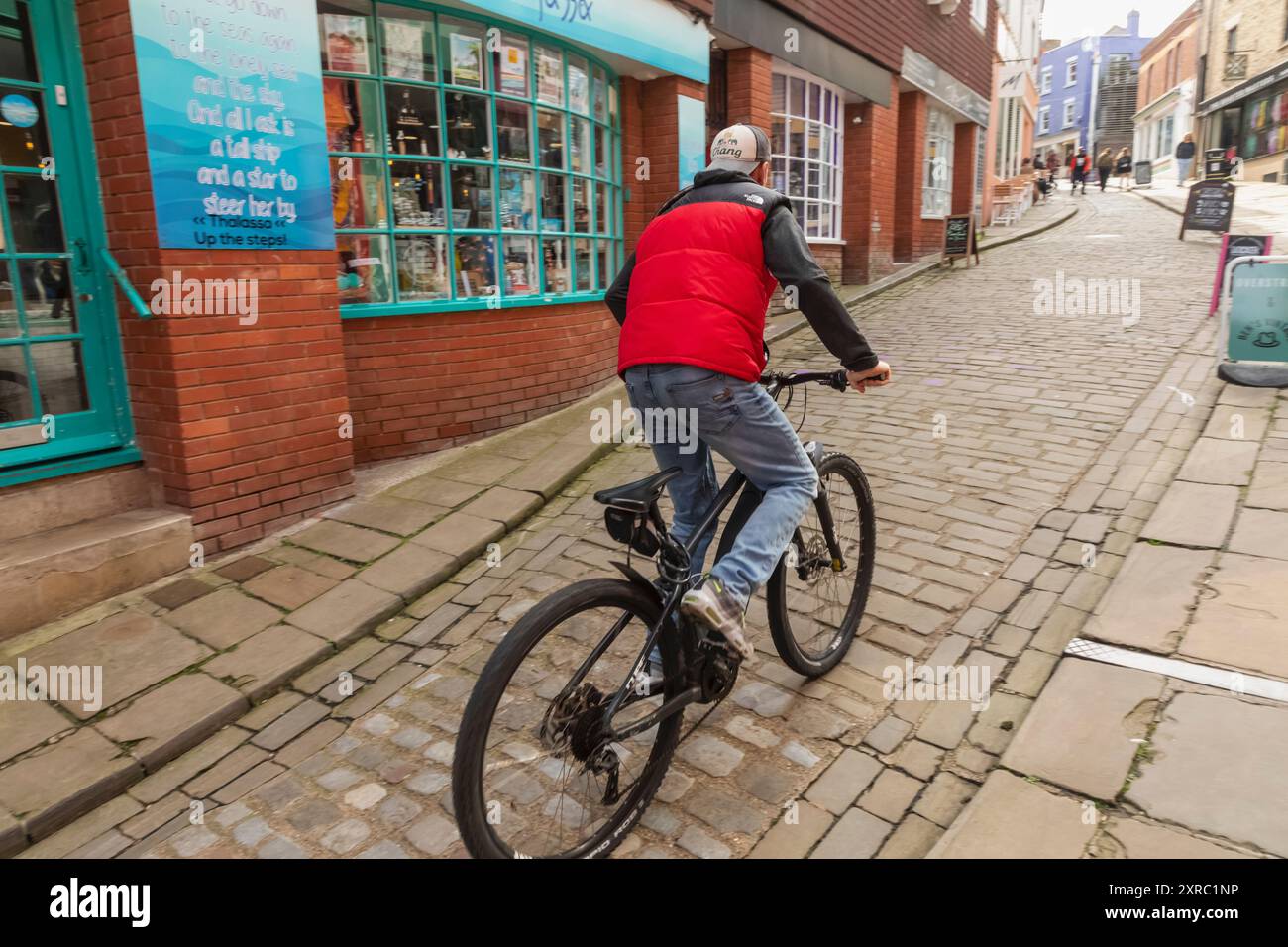 Inghilterra, Kent, Folkestone, The Creative Quarter, Cyclist Cycling Uphill nella Old High Street Foto Stock