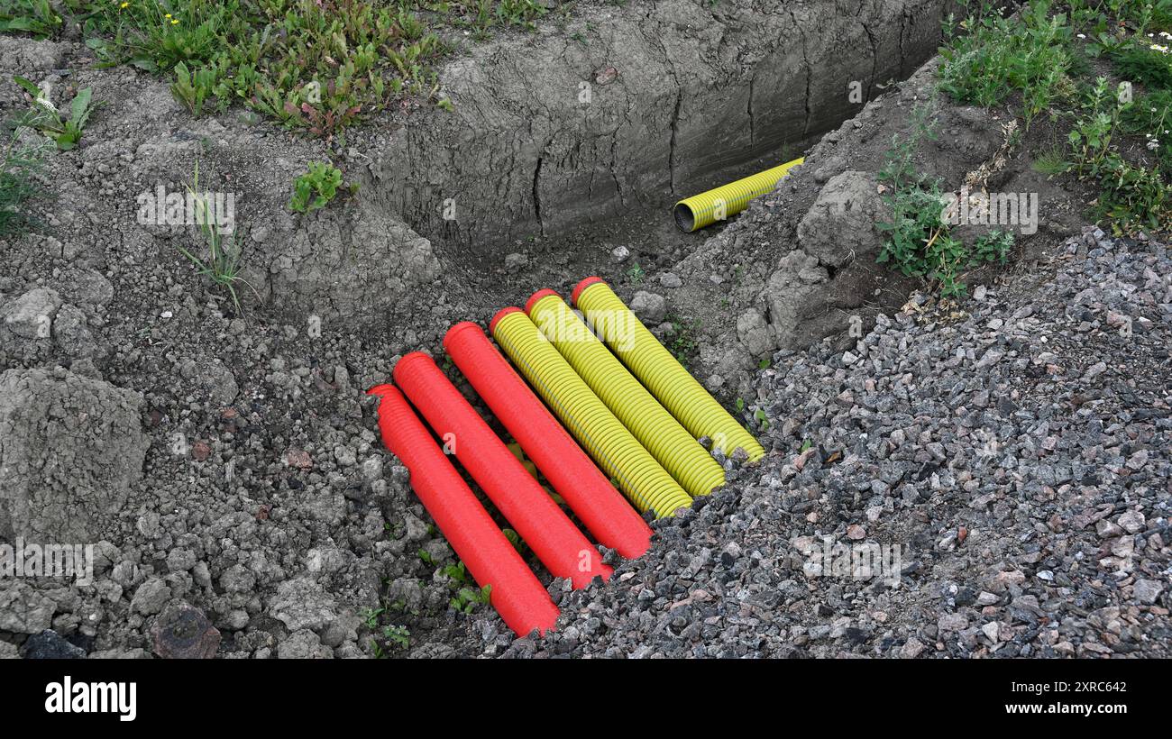 L'immagine mostra un cantiere con una trincea di scavo contenente tubi rossi e gialli dai colori vivaci, probabilmente per l'installazione di un'utilità o di un cavo Foto Stock