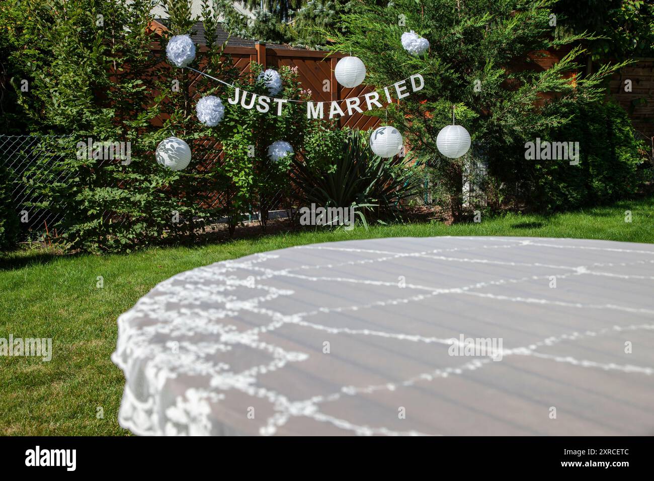 Tovaglia festosa sul tavolo in primo piano con uno striscione bianco e due parole inglesi in lettere maiuscole APPENA SPOSATE sullo sfondo, preparazioni per un matrimonio in giardino, matrimonio in estate Foto Stock