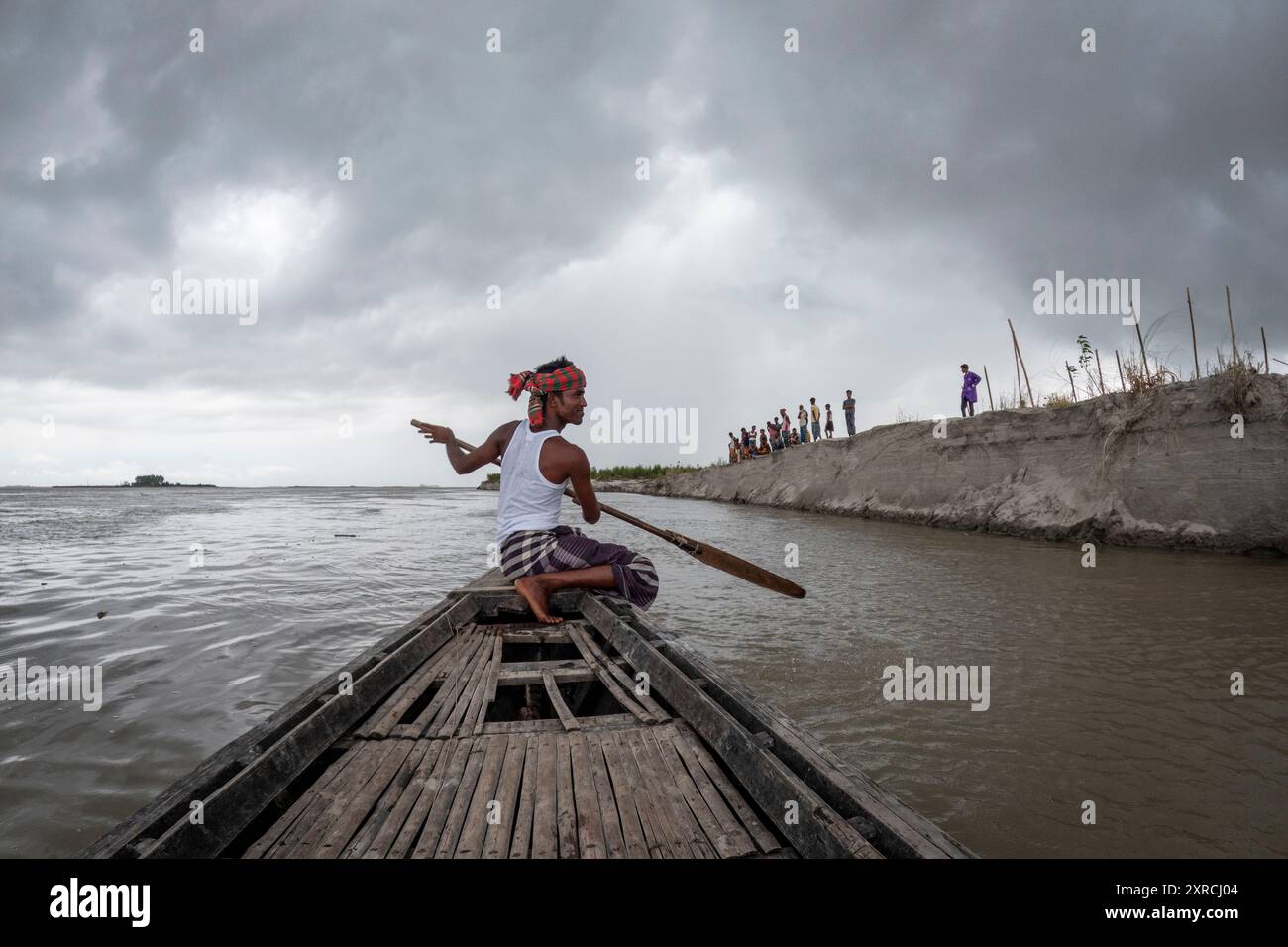 Rashed rema la sua barca di campagna a fianco degli abitanti del villaggio sul Kheyar Alga Char sul fiume Brahmaputra. L'ultima inondazione record ha invaso il char e ha lavato via tutti i loro raccolti e molte delle loro case. Da allora l'acqua è scesa, ma le colture sono sparite, così come grandi pezzi della loro terra. Foto Stock