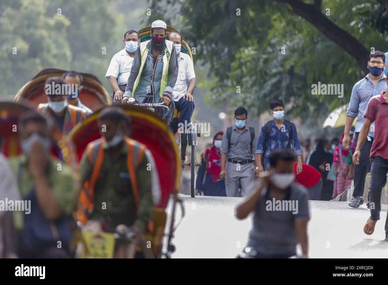 Persone che camminano o cavalcano risciò sul loro modo di lavorare nella corsa mattutina a Dhaka martedì 12 luglio. Il Bangladesh sta attraversando un'impennata di COVID-19, con un record di 13768 casi lunedì 12 luglio. Il 14 luglio, le restrizioni di blocco saranno attenuate per nove giorni per le celebrazioni Eid-ul-Azha. Foto Stock