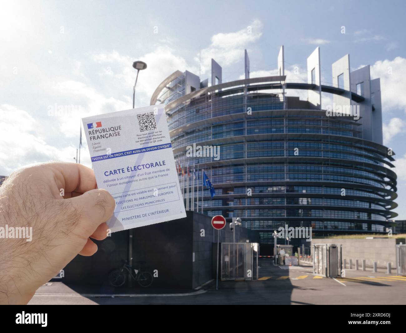 Strasburgo, Francia - 7 giugno 2024: Una persona tiene la parte posteriore di una carta elettorale francese, mostrando più fasce orarie di voto, davanti all'edificio del Parlamento europeo di Strasburgo, sottolineando l'attesa delle elezioni UE del 2024 Foto Stock