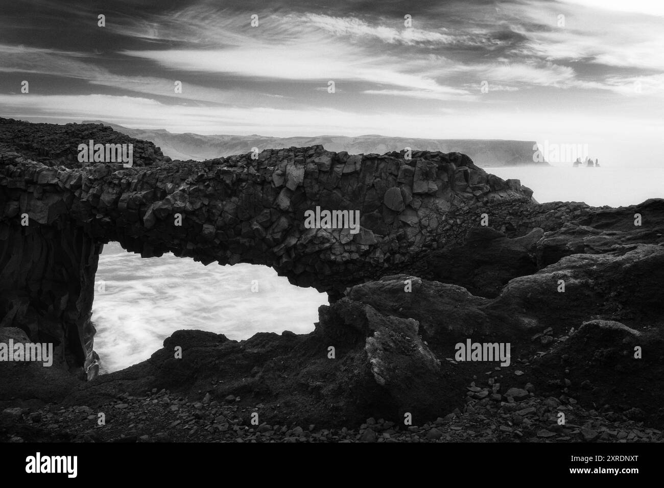 Le formazioni rocciose di Dyrholaey in Islanda, con Reynisdrangar sullo sfondo, belle arti in bianco e nero, nero scuro Foto Stock