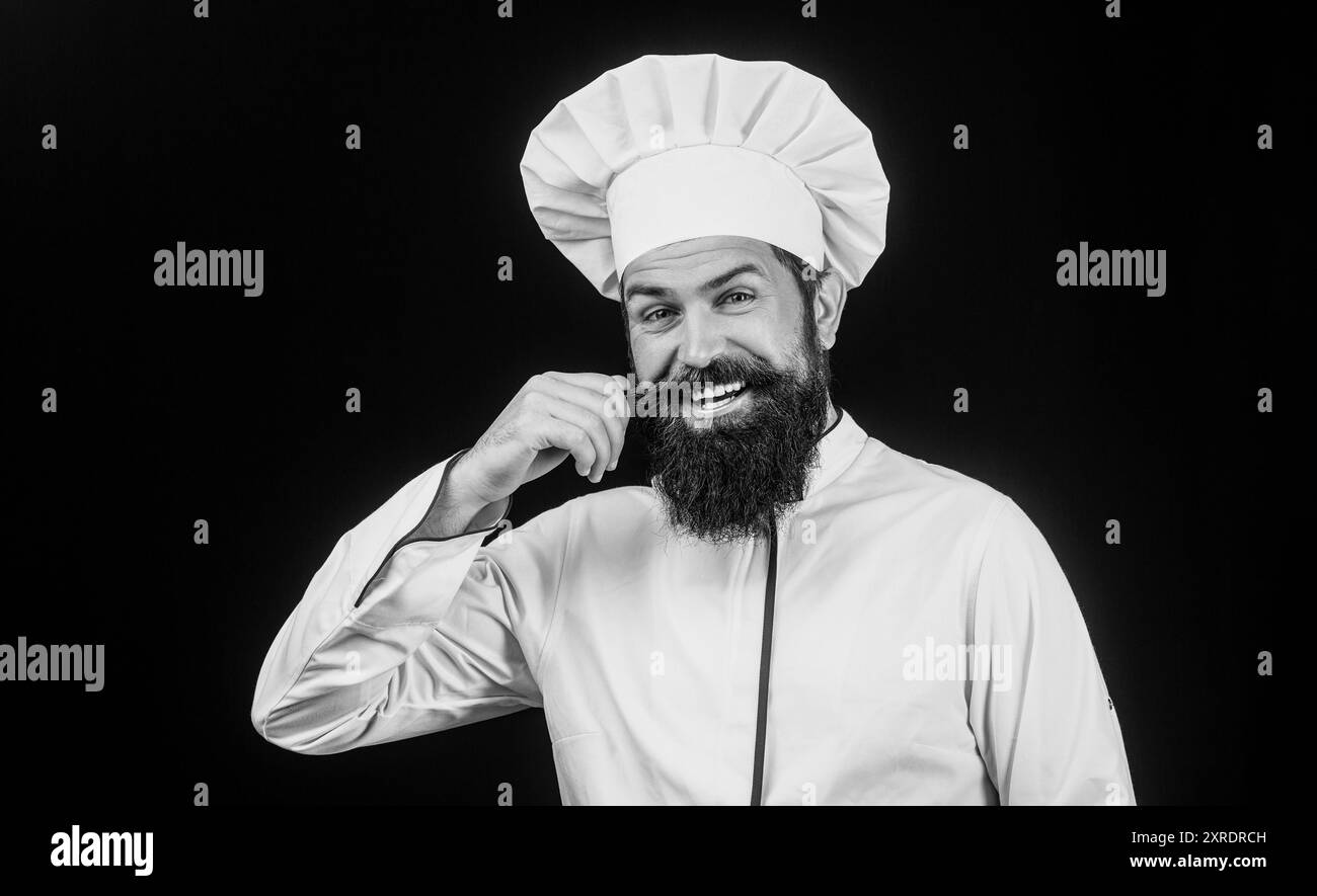 Giovane chef felice in uniforme su sfondo nero chiaro. Ritratto di un cuoco felice. Uomo barbuto in uniforme da chef. Chef professionista felice pronto Foto Stock