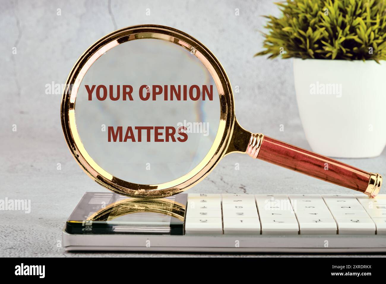Un cartello di testo che mostra LA TUA OPINIONE È IMPORTANTE sulla lente d'ingrandimento di fronte a una parete grigia, sfondo Foto Stock