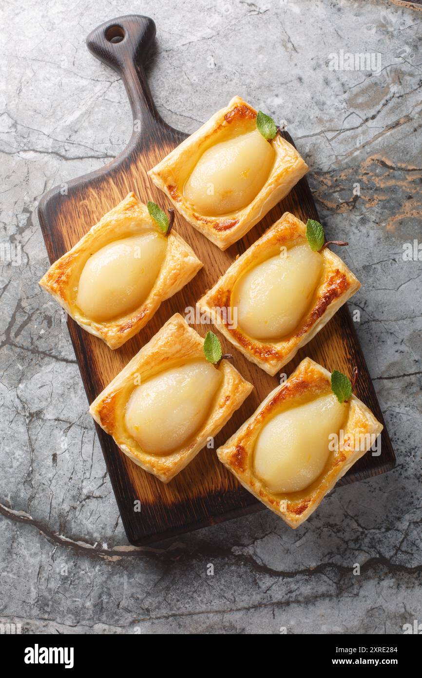 Pere autunnali cotte in pasta sfoglia e ripiene di noci e formaggio spalmabile sul bordo di legno sul tavolo. Vista dall'alto verticale Foto Stock