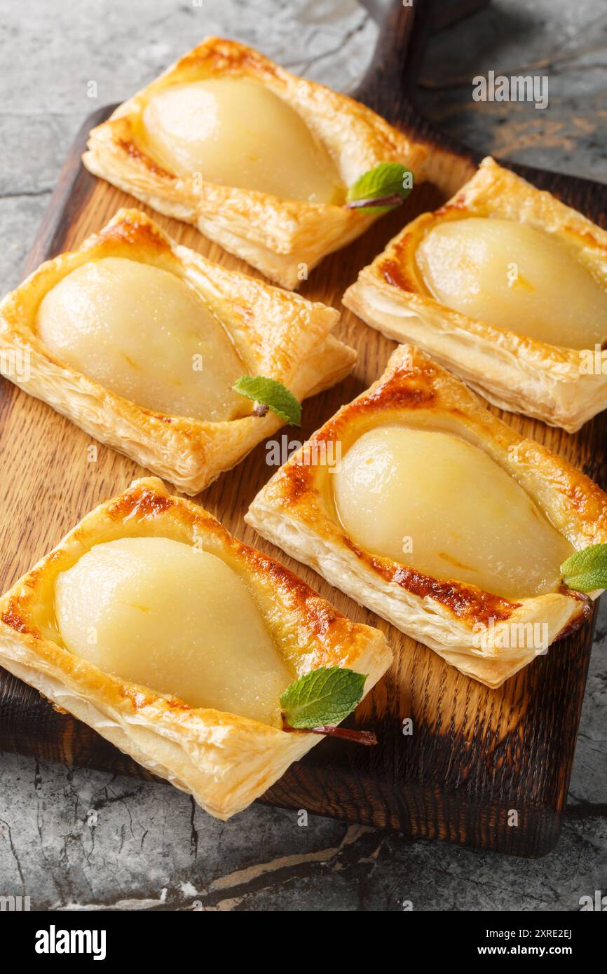 Pere autunnali cotte in pasta sfoglia e ripiene di noci e formaggio spalmabile sul bordo di legno sul tavolo. Verticale Foto Stock
