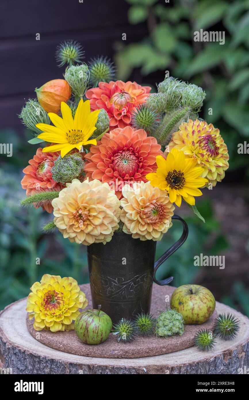 composizione floreale con dalie arancioni e gialle, girasoli, carote selvatiche, cardo e erbe in una tazza vintage di rame Foto Stock