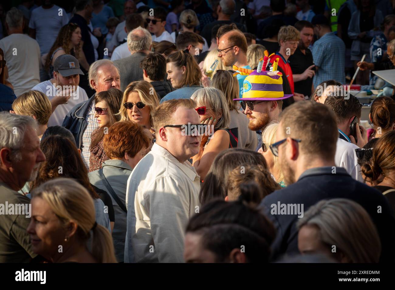 Uomo con cappello divertente a forma di torta con candele in una strada affollata del Lymm Village per il Lymm Festival Foodfest Foto Stock