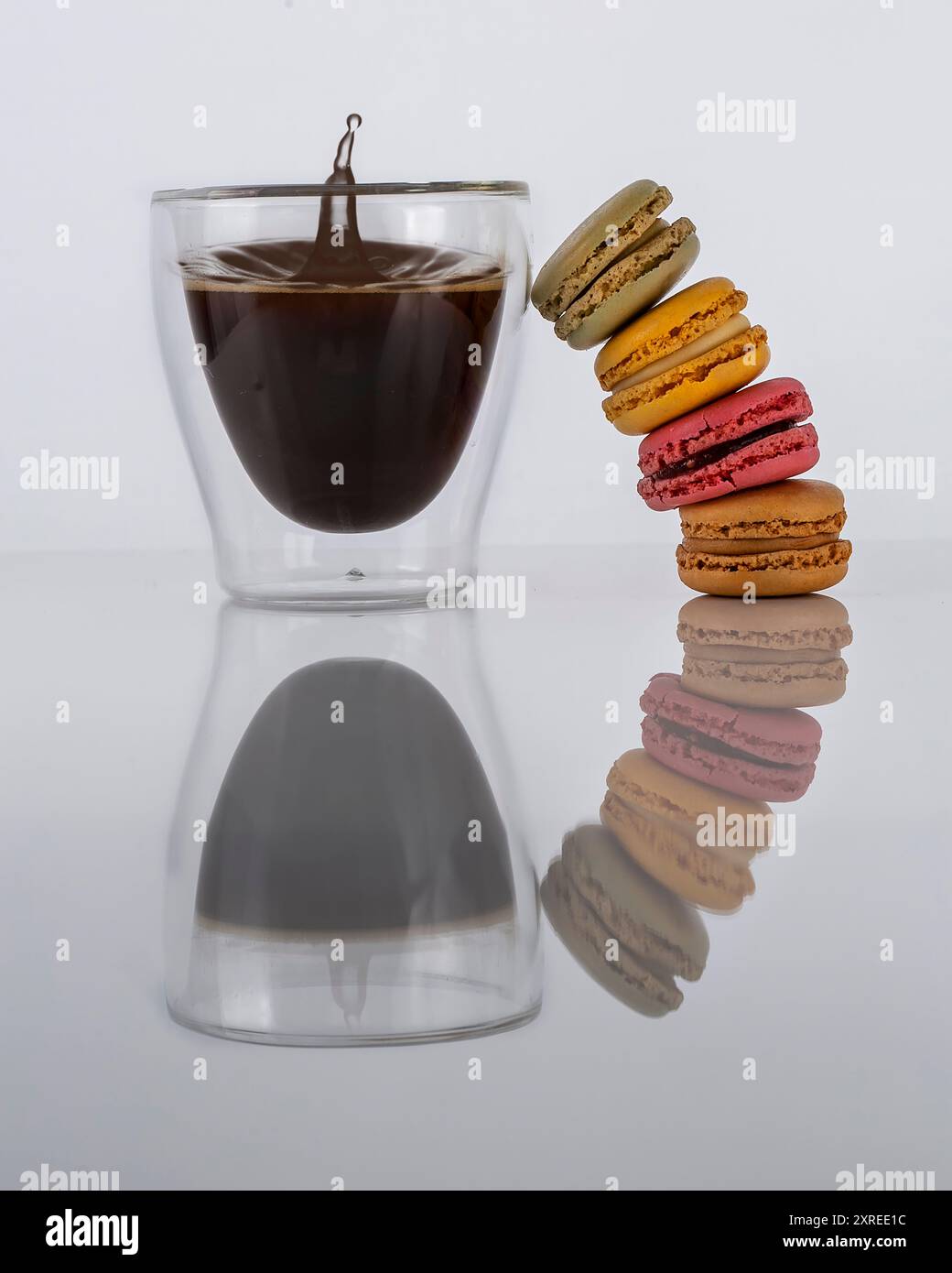 Macaron bilanciati su una tazza di caffè a doppia parete con una corona di caffè spruzzata Foto Stock