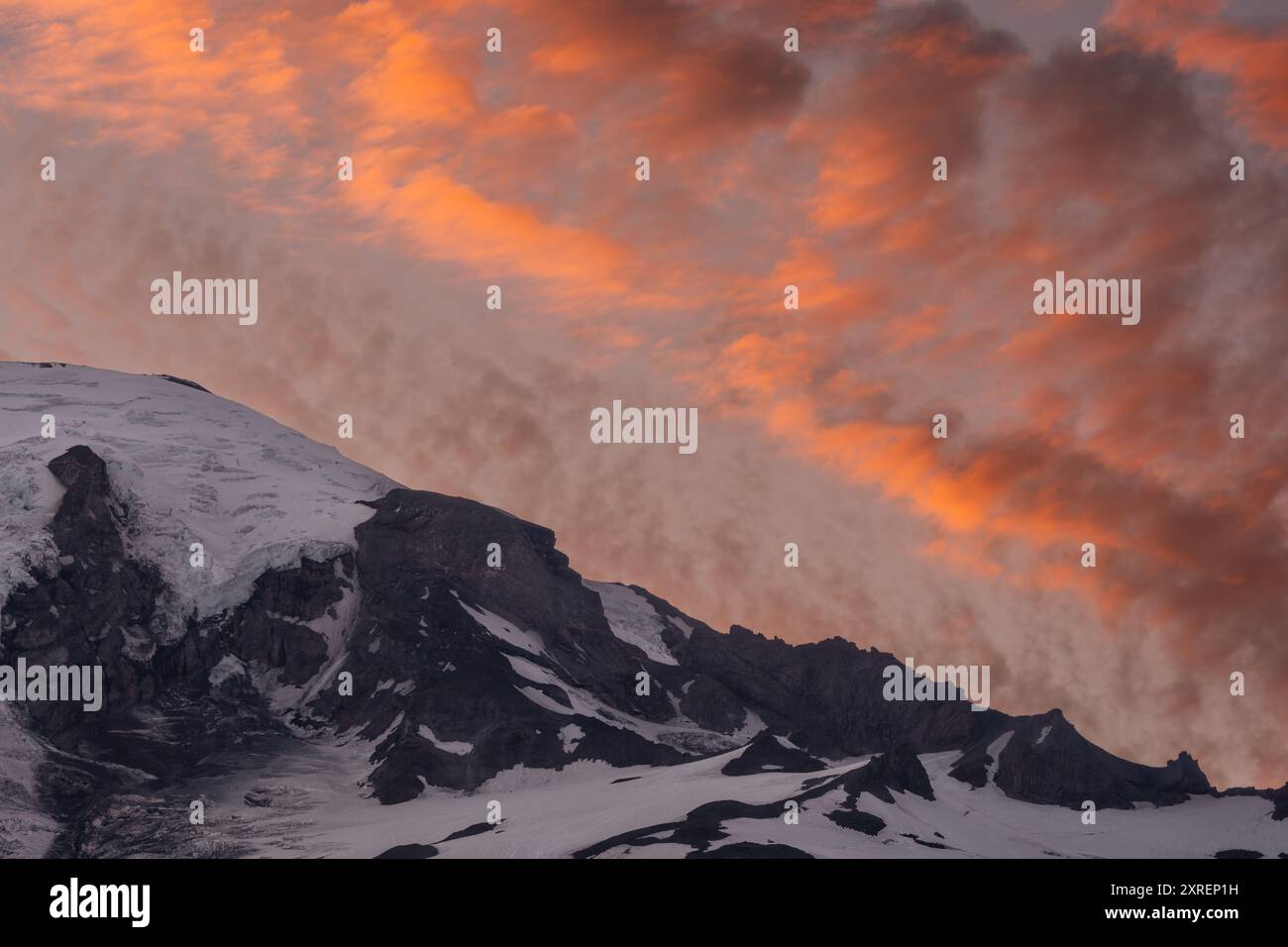 Le nuvole arancioni riempiono il cielo sopra Un primo piano del Monte Rainier Ridge al tramonto Foto Stock