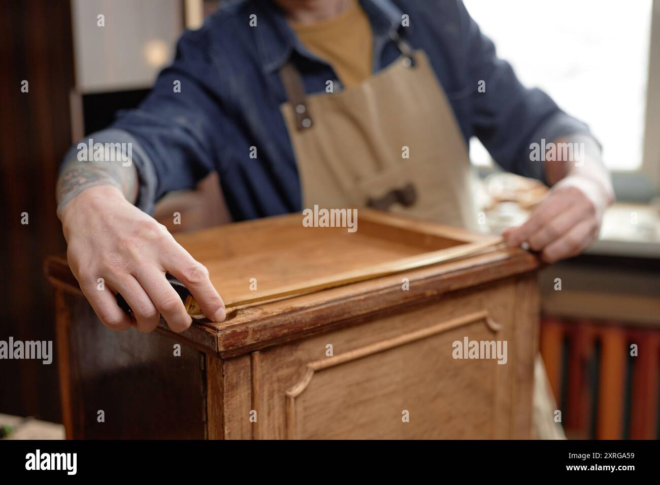 La persona che indossa un grembiule per la realizzazione di armadi in legno in officina con particolare attenzione alle mani e agli utensili utilizzati l'officina è ben illuminata con finestre che forniscono luce Foto Stock