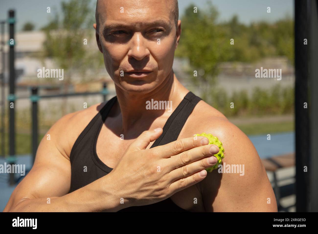 L'uomo degli atleti si massaggia le spalle con tecniche di palla da massaggio spiky per tenersi dopo l'allenamento attivo. Primo piano. Versione miofasciale. Foto Stock
