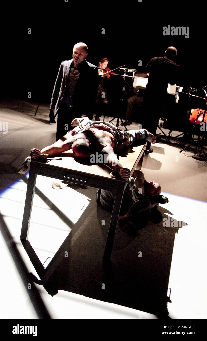 Posteriore: Michael Bennett (visitatore) in tavola: Omar Ebrahim (ufficiale) sotto tabella: Gerald Tyler (condannato uomo) in NELLA COLONIA PENALE al Linbury Studio Theatre, The Royal Opera, Covent Garden, Londra WC2 15/09/2010 a Music Theatre Galles musica di produzione: Philip Glass libretto: Rudolph Wurlitzer basato sulla storia di Kafka direttore: Michael Rafferty design: Simon Banham lighting: ACE McCarron regista: Michael McCarthy Foto Stock