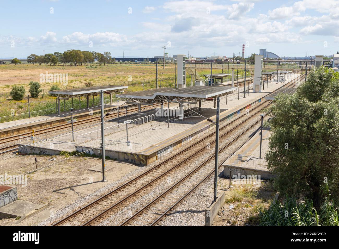 Stazione ferroviaria vuota con binari in acciaio che conducono a un'area industriale con un cielo blu e soffici nuvole bianche Foto Stock Stazione ferroviaria vuota con binari in acciaio che conducono a un'area industriale con un cielo blu e soffici nuvole bianche Foto Stock