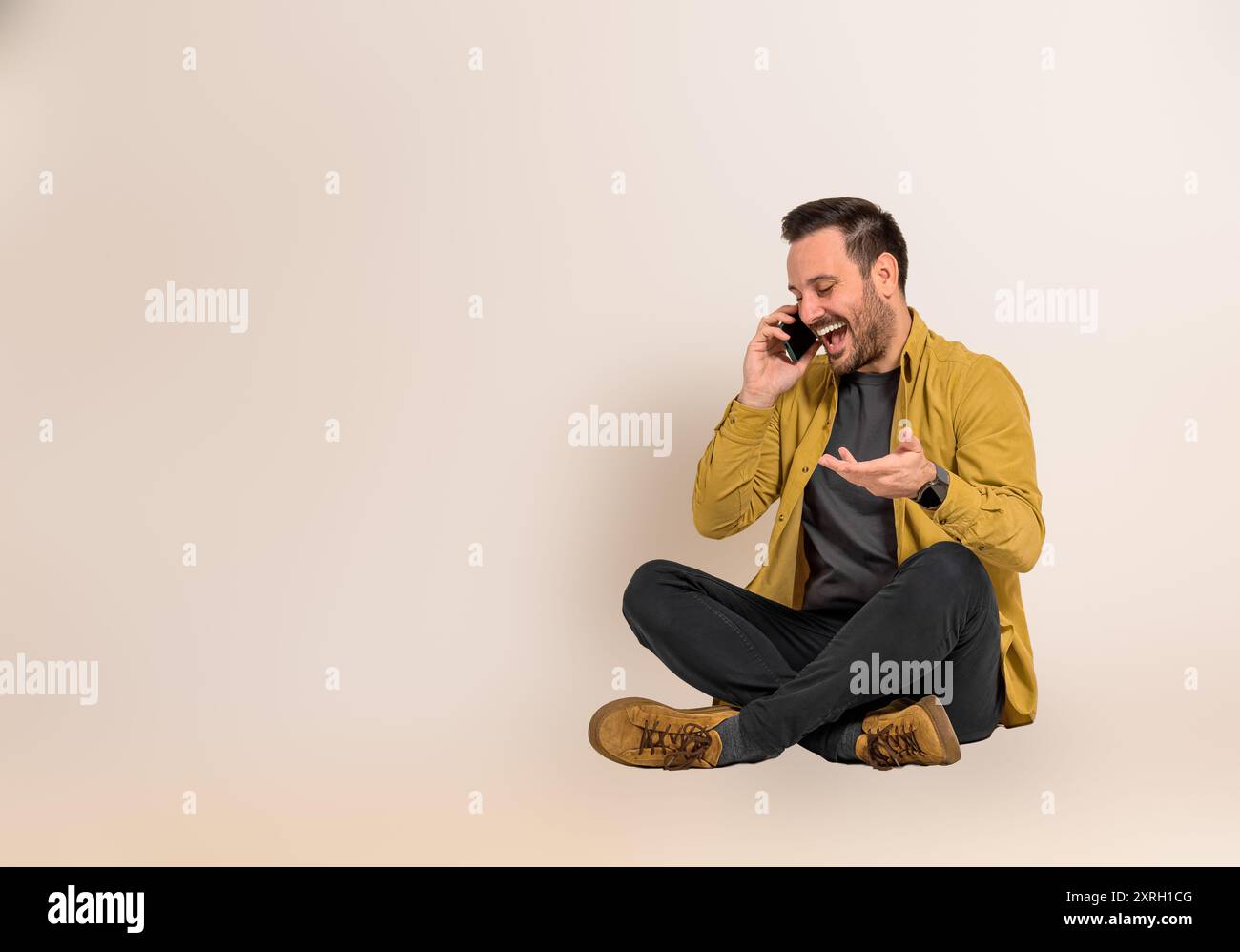 Allegro giovane uomo d'affari che ride e comunica con il cliente tramite smartphone mentre è seduto con le gambe incrociate. Il responsabile delle vendite parla sul cellphon Foto Stock