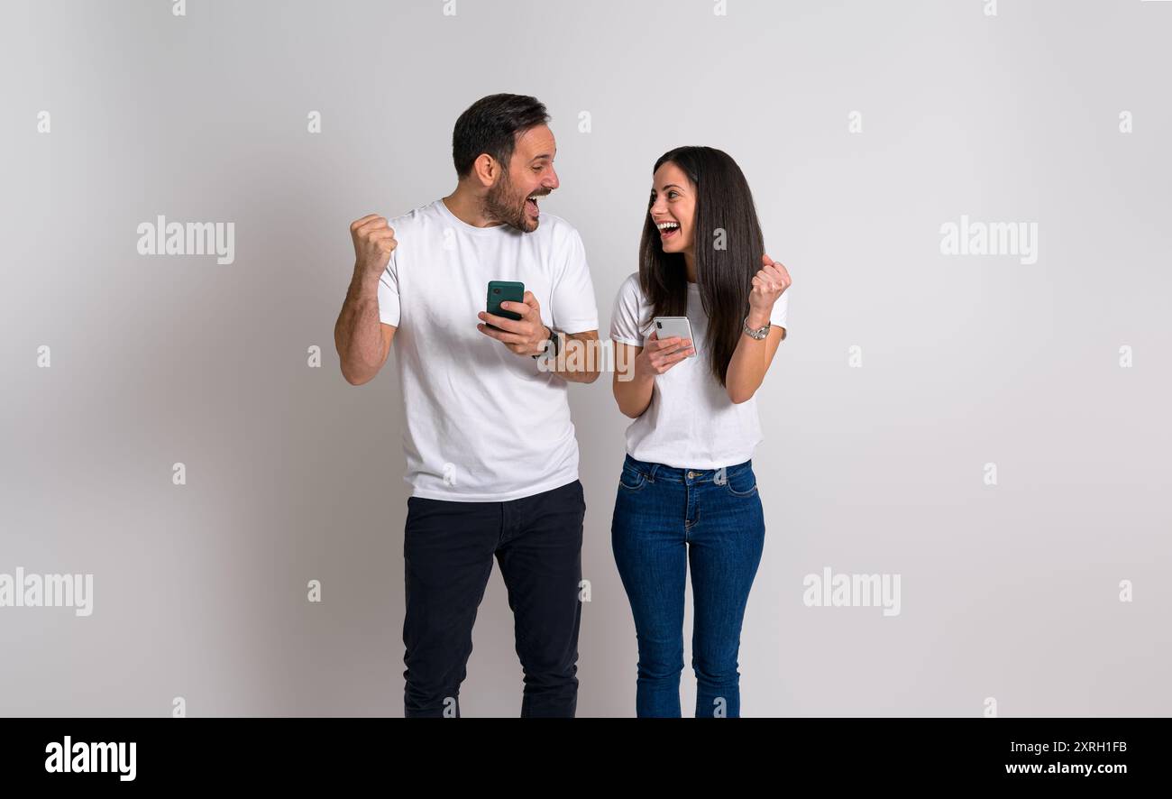 Una giovane coppia che puzza pugni e urla eccitante dopo aver ricevuto notizie sulle merci tramite smartphone. Uomo e donna estatici che si guardano felicemente Foto Stock