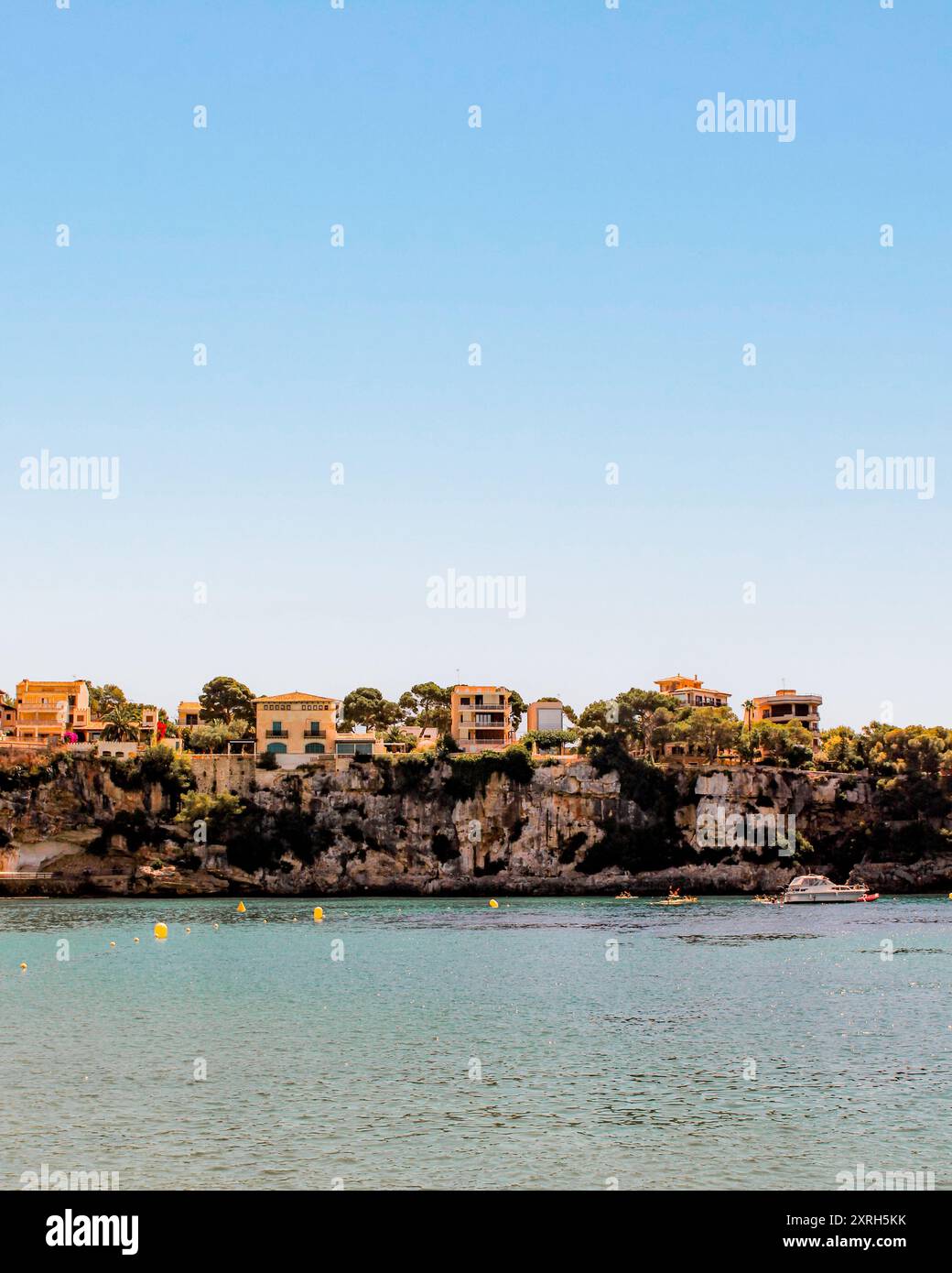 Una splendida vista sulla scogliera delle case mediterranee che si affacciano sulle calme acque turchesi, sotto un cielo azzurro Foto Stock
