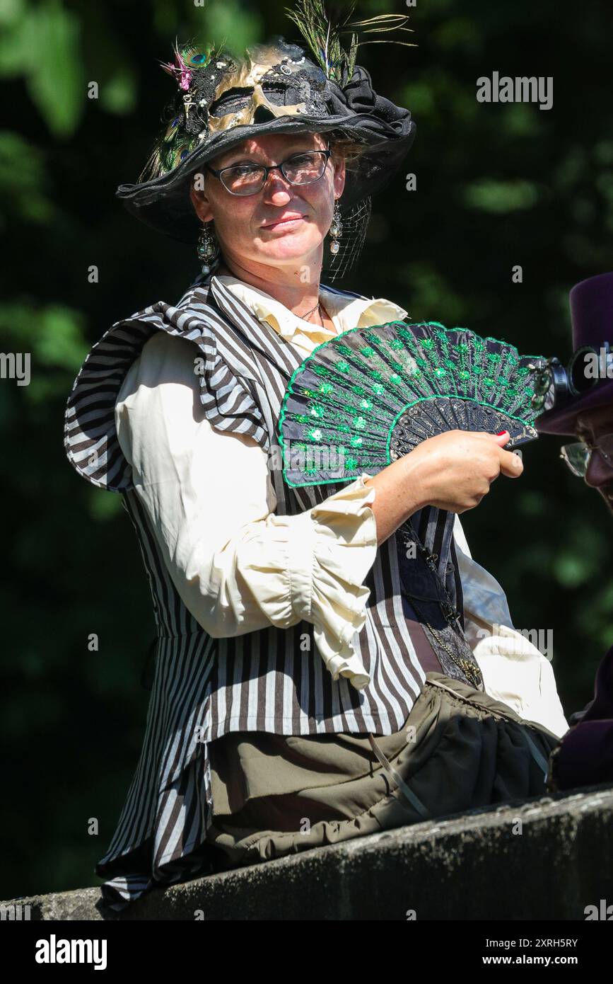 Henrichenburg, Waltrop, Germania. 10 agosto 2024. Un ventilatore vittoriano è utile a 30 gradi di temperatura. I fan dello steampunk, i gruppi e i visitatori, molti in costumi d'epoca retrò-futuristica o vittoriana, si divertiranno il primo giorno dell'annuale festival e mercato del Giubileo di Steampunk. Quest'anno, il festival coincide con il 125° anniversario dello storico impianto di risalita di Henrichenburg Boat Lift, sito patrimonio industriale lungo il canale Dortmund-EMS. Crediti: Imageplotter/Alamy Live News Foto Stock