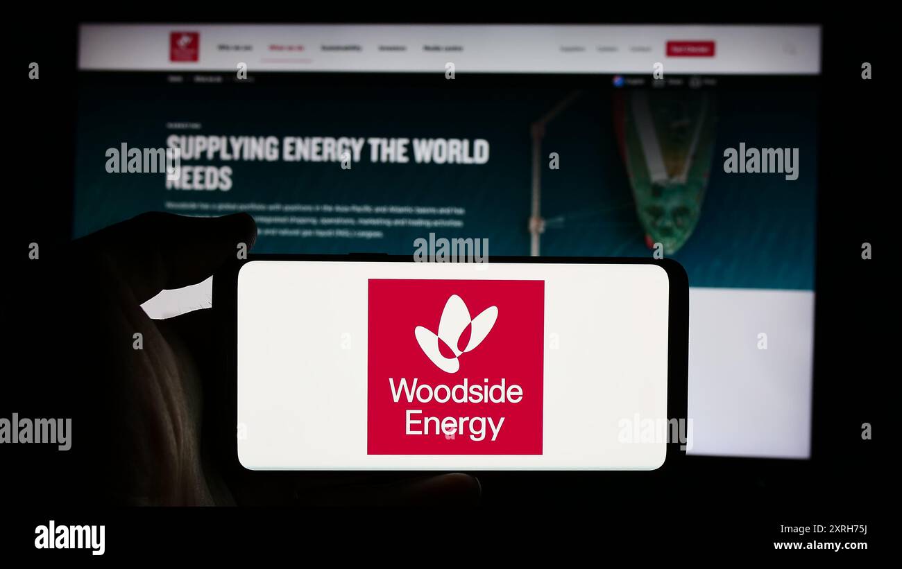 Persona che detiene un cellulare con il logo della società australiana Woodside Energy Group Limited di fronte alla pagina Web aziendale. Mettere a fuoco il display del telefono. Foto Stock